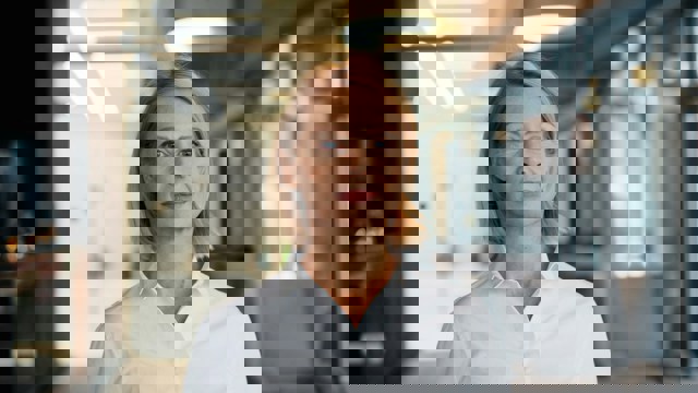 Foto av kvinna i vit skjorta tittar in i kameran.