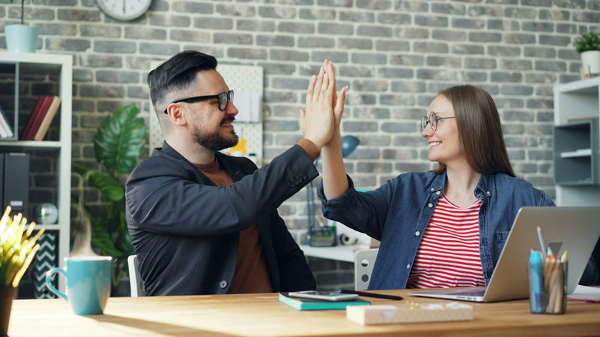 Två personer sitter vid ett skrivbord med en laptop och gör en high five.